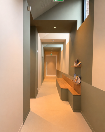 Couloir aux plafonds vert sauge et banquette en bois dans une maison médicale à Faches-Thumesnil